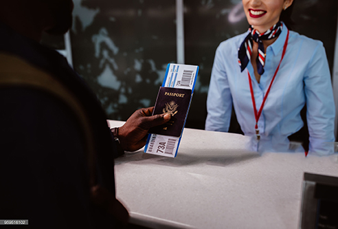 Close-up of man's hand holding passport and boarding pass at airline check-in desk at airport