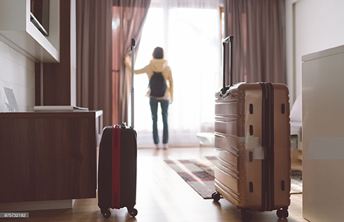 Rear view of tourist in the hotel room pulling the curtains to see the view